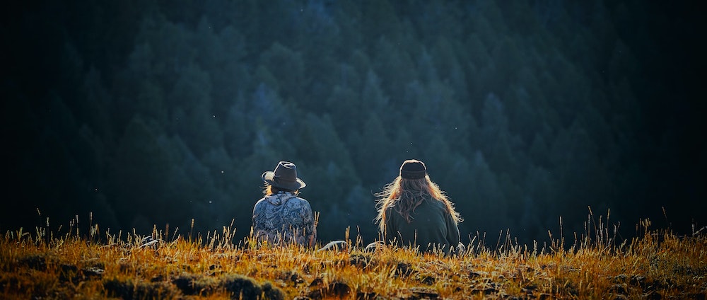 Twee mensen zitten naast elkaar in de natuur, je ziet ze in de verte op de rug